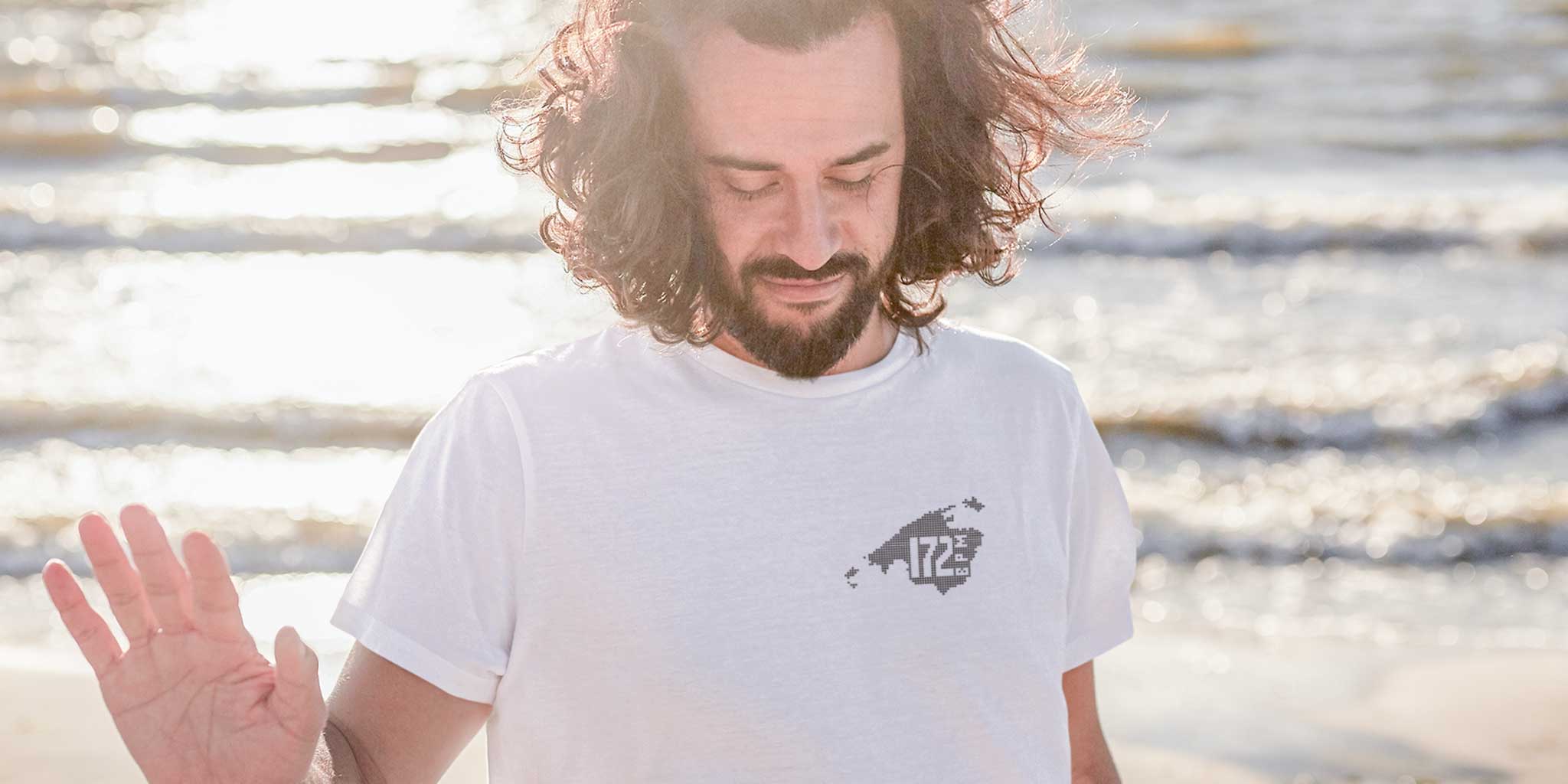A man with long hair walking by the sea wearing a Balearic Breaks 172 BPM oversized t-shirt